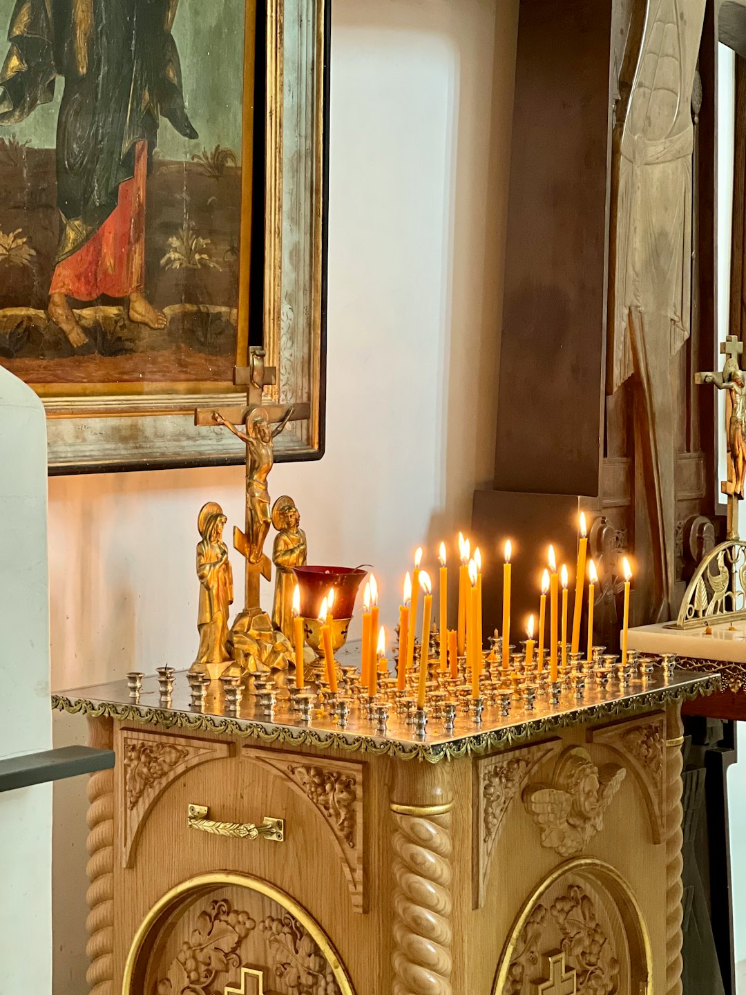 Lit candles glow on a wooden stand in a church.