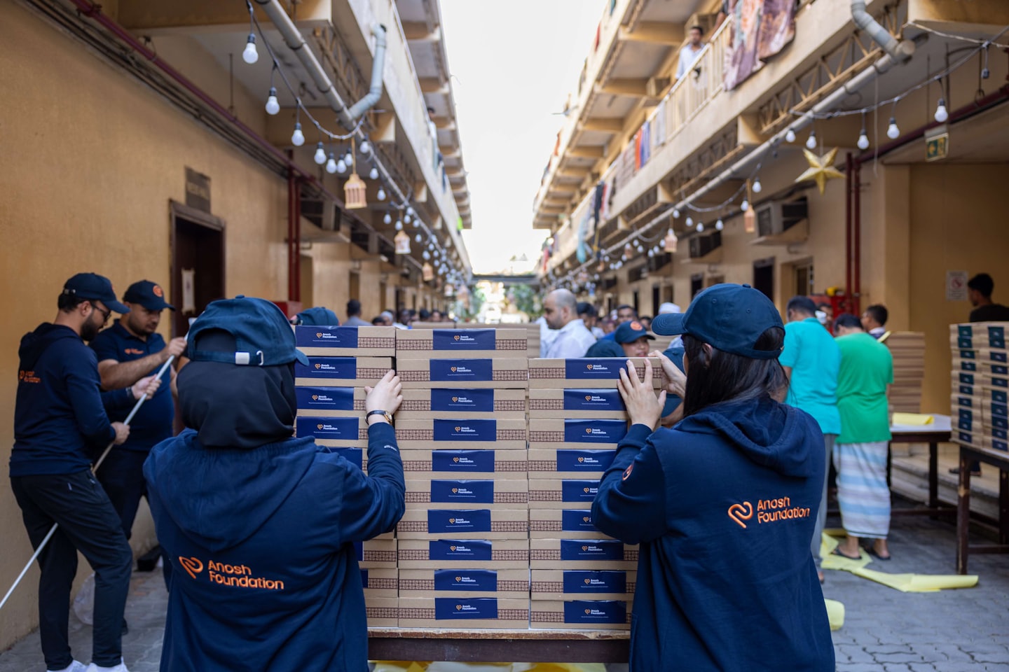 Volunteers stack and distribute cardboard boxes outdoors between buildings.