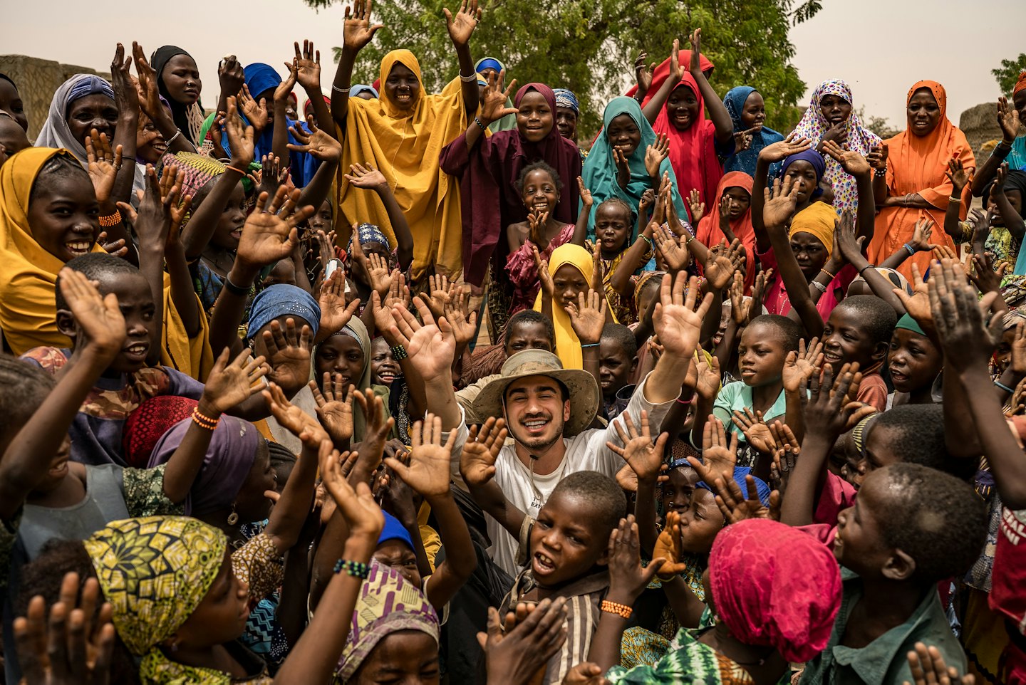 A group of people smiling and raising their hands outdoors.