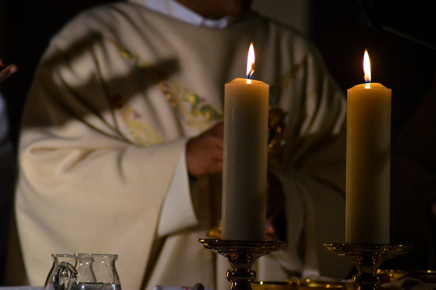 Two lit candles in ornate gold holders on a surface.