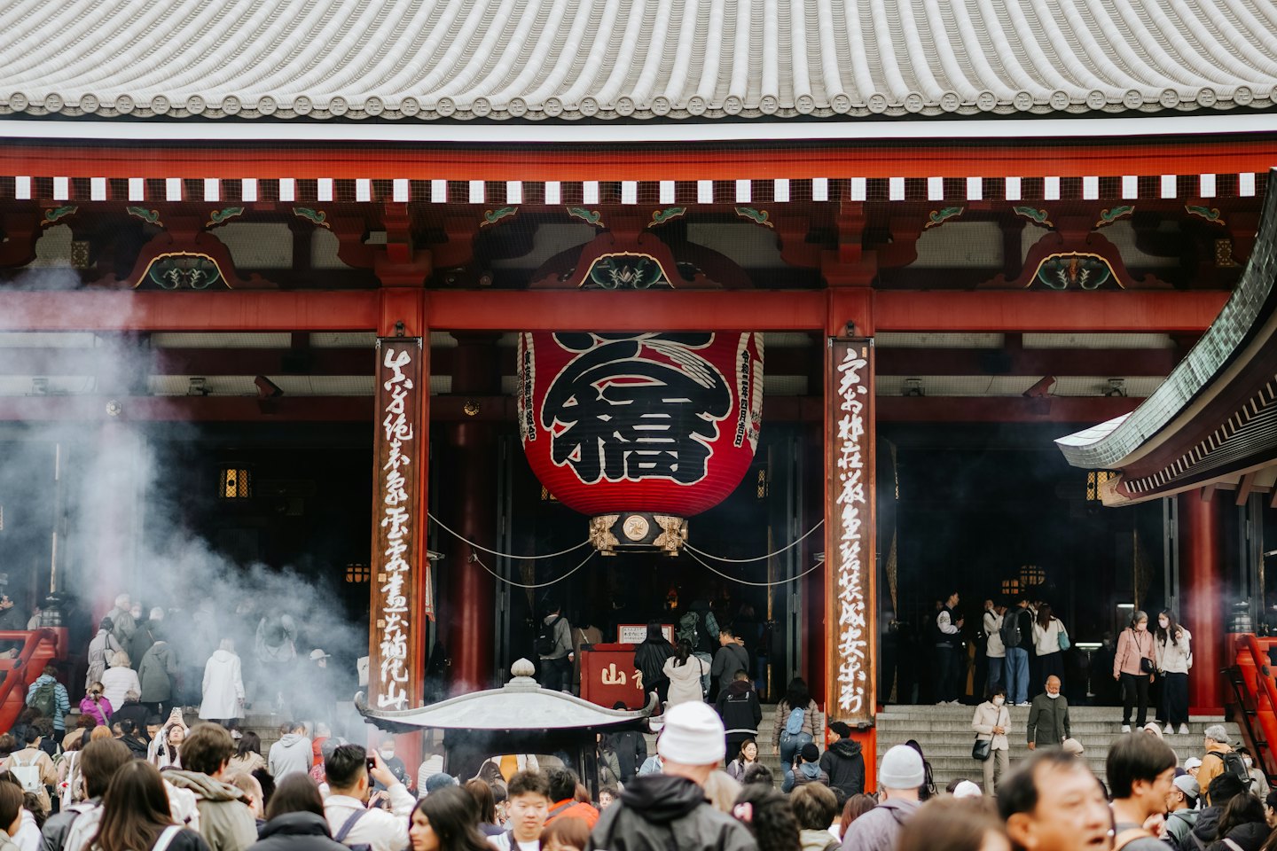 Crowds gather before a traditional temple with a red lantern.