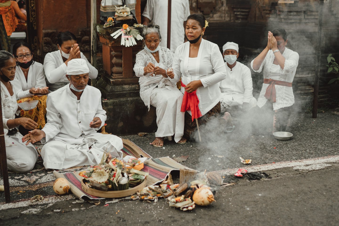 People in white traditional clothing at an outdoor spiritual ceremony.