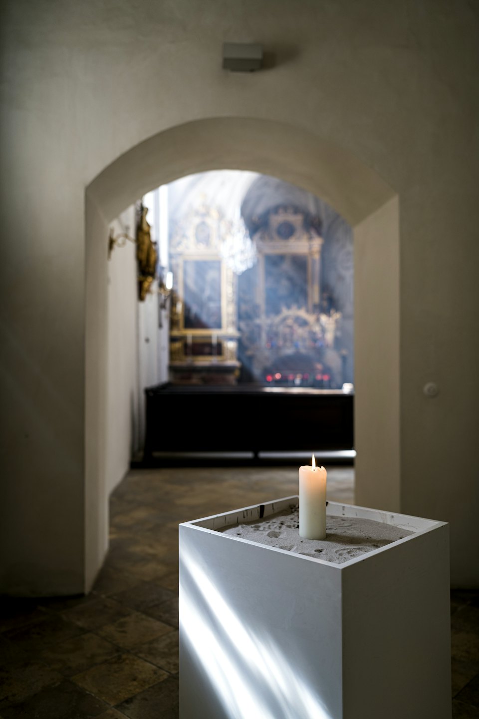 A single white candle glows in a square container.