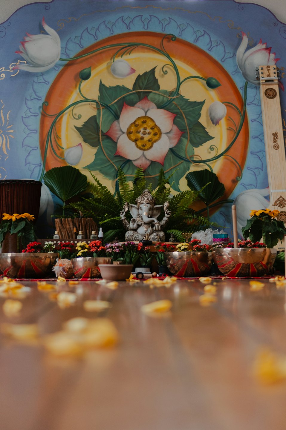 Ganesha statue with flowers and instruments arranged on a wooden floor.